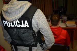 policjant przyprowadził zatrzymanego mężczyznę na czynności i zatrzymany siedzi na krześle