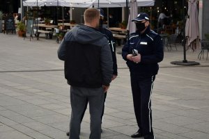 Umundurowane policjantki na deptaku rozmawiają z mężczyzną. W tle witryny lokali i ogródki przed lokalami. Zdjęcie archiwalne.