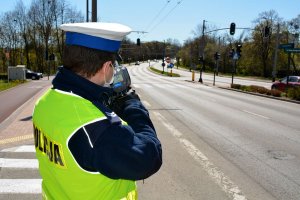 umundurowany policjant za pomocą urządzenia mierzy prędkość pojazdów jadących ulicą