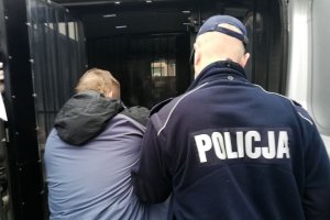 umundurowany policjant wprowadza zatrzymanego mężczyznę do radiowozu