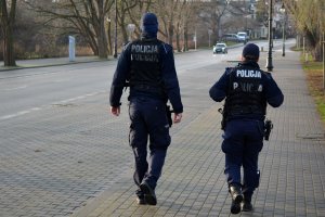 umundurowani policjanci idą chodnikiem wzdłuż ulicy, po której jadą samochody