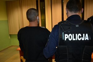 Pomieszczenie Komendy Miejskiej Policji w Sopocie - umundurowany policjant prowadzi zatrzymanego mężczyznę