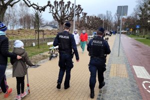 Umundurowani policjanci idą deptakiem dla pieszych. Obok idą inne osoby.