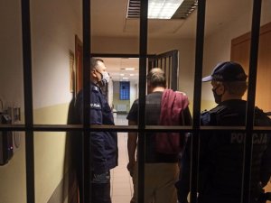 Umundurowani policjanci wprowadzają do pomieszczenia dla osób zatrzymanych mężczyznę