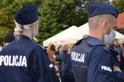 Na zdjęciu dwoje umundurowanych policjantów z maseczkami na twarzy. Za nimi widać fragment namiotu i sylwetki osób.