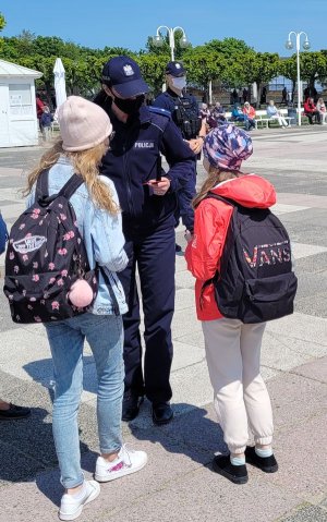 Plac. Umundurowana policjantka rozmawia z dziećmi.