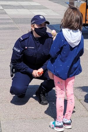 Umundurowana policjantka rozmawia z dzieckiem na placu.