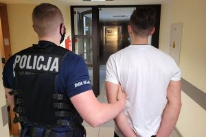 Umundurowany policjant prowadzi zatrzymanego mężczyznę