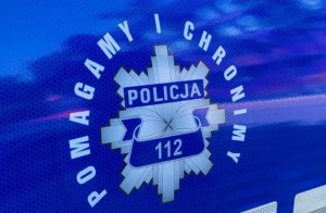 Fragment radiowozu. Na karoserii logo policyjne z napisami POLICJA, 112, POMAGAMY I CHRONIMY.