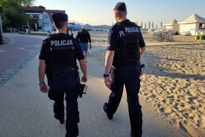 Dwaj umundurowani policjanci idą chodnikiem wzdłuż plaży