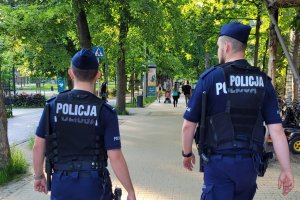 Dwaj umundurowani policjanci idą chodnikiem wzdłuż pasa nadmorskiego