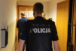 Umundurowany policjant wprowadza do pomieszczenia dla osób zatrzymanych mężczyznę.