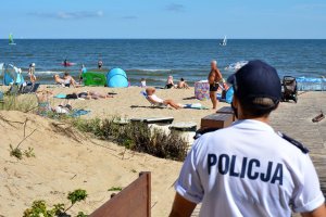 Umundurowana policjantka obserwuje rejon plaży, na której wypoczywają osoby.