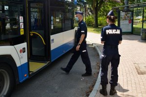 Przystanek autobusowy. Umundurowani policjanci wchodzą do autobusu miejskiego.