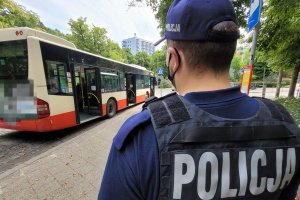 Umundurowany policjant obserwuje osoby przebywające na zatoczce autobusowej i siedzące w autobusie.