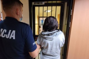 Umundurowany policjant prowadzi do pomieszczenia zatrzymaną kobietę