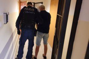 Umundurowany policjant prowadzi korytarzem zatrzymanego mężczyznę