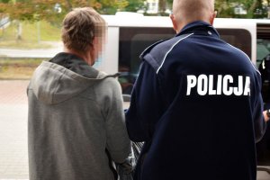 Policjant prowadzi do pojazdu zatrzymanego mężczyznę