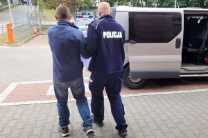 Policjant prowadzi w stronę pojazdu zatrzymanego mężczyznę