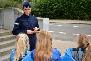 Umundurowana policjantka rozmawia z dziećmi. Za nimi widoczna ulica.