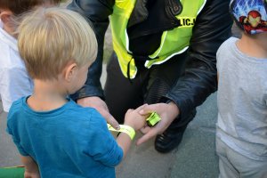 Umundurowany policjant zakłada dziecku na rękę opaskę odblaskową