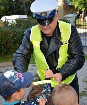 Umundurowany policjant zakłada dziecku na rękę opaskę odblaskową