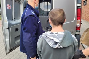 Umundurowany policjant prowadzi do pojazdu zatrzymanego mężczyznę