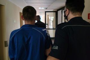 Policjant prowadzi korytarzem zatrzymanego mężczyznę.