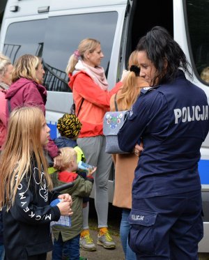 Grupa dzieci wchodzi do radiowozu, przy którym stoją policjantki umundurowane.