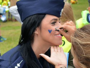 Kobieta maluje na policzku umundurowanej policjantki niebieskie serce