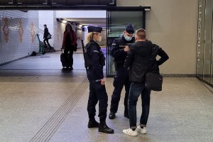 Umundurowani policjanci na holu dworca rozmawiają z mężczyzną. Za nimi widoczne w oddali dwie inne osoby.