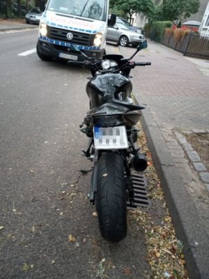 Na zdjęciu motocykl, a za nim widoczny ambulans. Oba pojazdy stoją na jezdni.