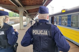 Umundurowani policjanci na dworcu kolejowym. Za nimi widoczny pociąg z otwartymi drzwiami