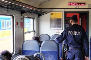 Dwaj umundurowani policjanci idą przez przedział pociągu. Na siedzeniach widoczne sylwetki osób.