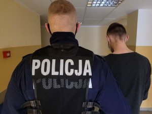 Umundurowany policjant prowadzi korytarzem zatrzymanego mężczyznę.