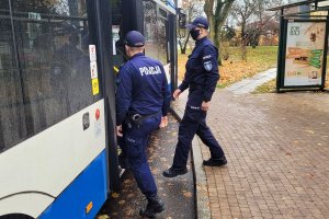 Dwaj umundurowani policjanci wchodzą do autobusu komunikacji miejskiej.