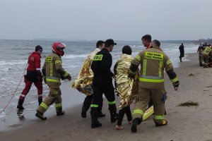 Plaża. Umundurowani ratownicy wodni, strażacy, policjant i kobieta idą plażą