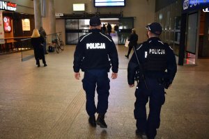 Umundurowani policjanci idą przez hol budynku. Obok nich spacerują inne osoby.