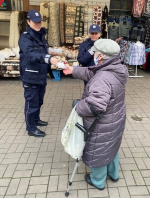 Umundurowane policjantki wręczają maseczkę starszej kobiecie.