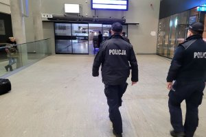 Umundurowani policjanci idą przez hol budynku. W tle widać inne osoby.