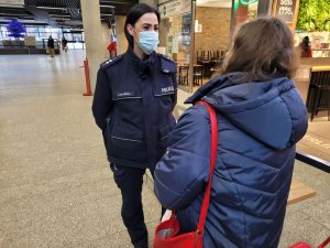 Wnętrze budynku. Umundurowana policjantka rozmawia z kobietą. Za nimi w tle lokale.