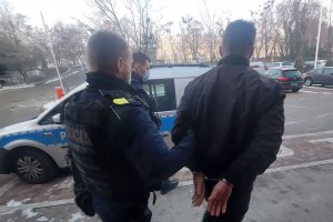 Umundurowani policjanci prowadzą do oznakowanego radiowozu zatrzymanego mężczyznę.