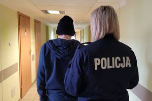 Umundurowana policjantka prowadzi korytarzem zatrzymanego mężczyznę.