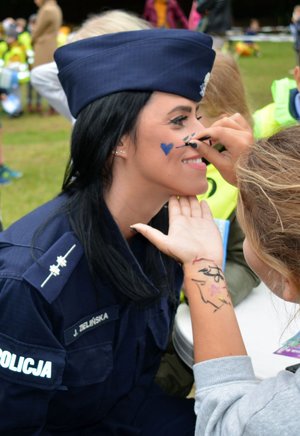 Festyn. Dziewczyna w stroju cywilnym maluje niebieskie serce na policzku umundurowanej policjantki