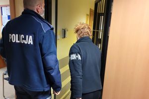 Umundurowany policjant wprowadza do pomieszczenia dla osób zatrzymanych kobietę.