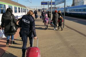 Peron dworca kolejowego. Umundurowani policjanci idą razem z innymi osobami i pomagają w niesieniu ich bagaży.