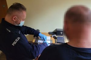 Umundurowany policjant wykonuje czynności z zatrzymanym mężczyzną