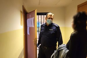 Pomieszczenie dla osób zatrzymanych. Umundurowany policjant rozmawia z zatrzymaną kobietą.