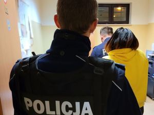 Umundurowany policjant wchodzi do pomieszczenia. Przed nim wszedł tam drugi umundurowany policjant i kobieta w stroju cywilnym