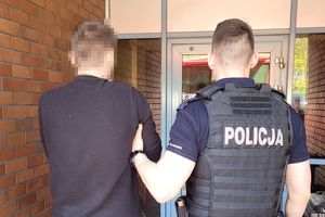 Umundurowany policjant prowadzi zatrzymanego mężczyznę